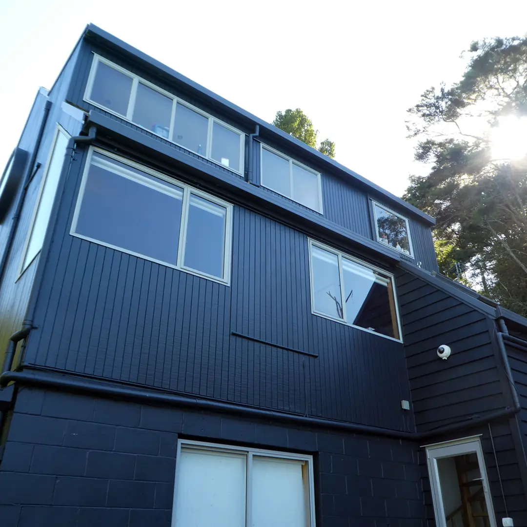 The image is of a house with windows, taken after exterior painting. It features a clear sky, outdoor setting, and a tree nearby.