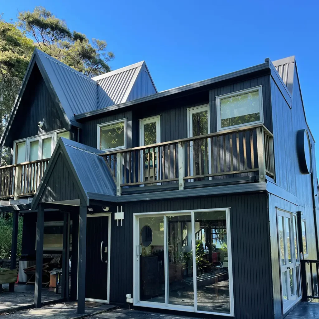 The picture shows the exterior of a darkened house that has been painted with Weathershield® ColourGuardTM Rawene. It has features like vertical cladding, a deck, aluminium windows, and round windows.