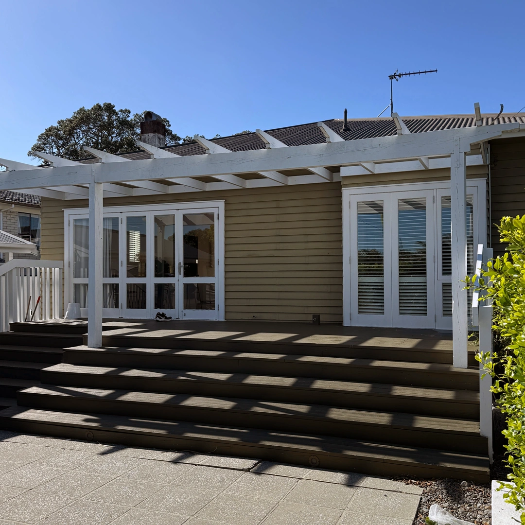 The image showcases a beautifully painted house exterior with a fresh and elegant look. The walls are coated in a smooth, neutral shade, enhancing the home's timeless architectural style. Crisp white trim and window frames provide a striking contrast, adding depth and sophistication. The front entrance appears inviting, with a well-maintained pathway leading to the door. The surrounding landscape is neatly arranged, complementing the freshly painted exterior. The high-quality finish and attention to detail reflect expert craftsmanship, significantly boosting the home's street appeal.