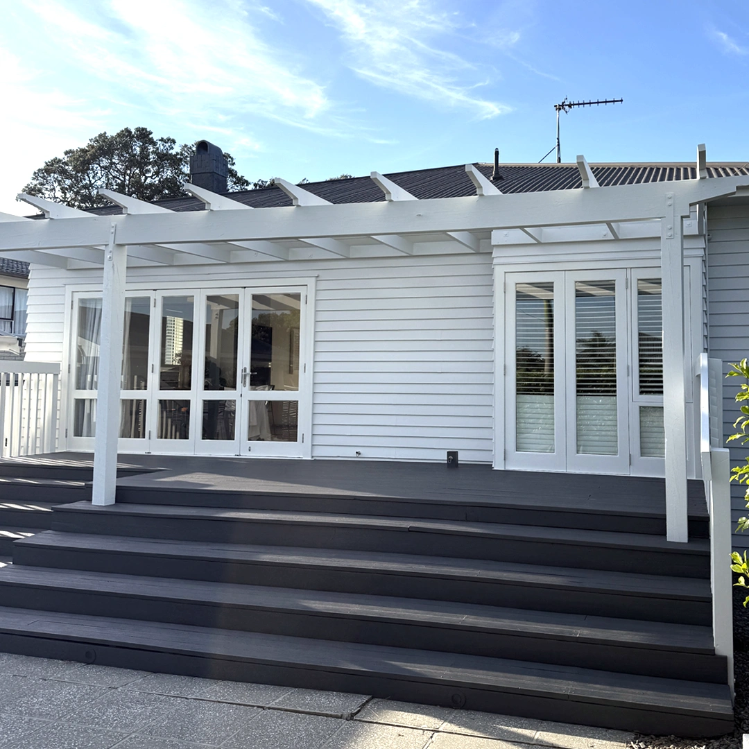 The image showcases a stunningly painted home exterior with a fresh and modern look. The walls are finished in a smooth, neutral color, enhancing the home's classic architectural style. The crisp white trim and window frames provide a beautiful contrast, adding elegance and definition. The front door stands as a welcoming focal point, complementing the overall design. The surrounding landscaping is well-maintained, further elevating the home's street appeal. The flawless paint job reflects high-quality craftsmanship, giving the house a refreshed and polished appearance.