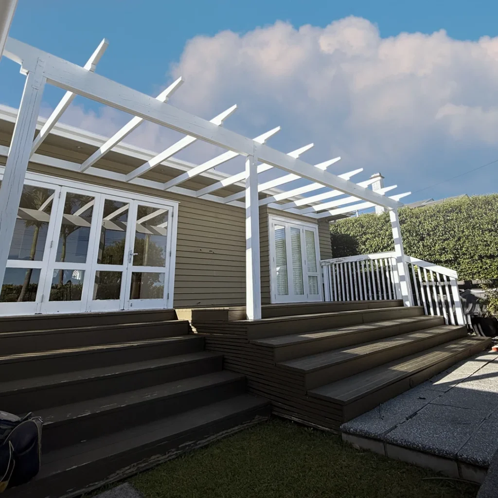 The image shows a well-kept house façade in Bayswater, Auckland. The fresh layer of paint emphasises the home's architectural characteristics, giving it a clean, modern, and stylish appearance. The walls are painted in a smooth, neutral tone that is nicely offset by crisp white trim and window frames, which provide contrast and elegance. The doorway is inviting and complements the renovated exterior. The beautiful finish demonstrates excellent craftsmanship, considerably boosting the home's street appeal while remaining well-kept and fashionable.