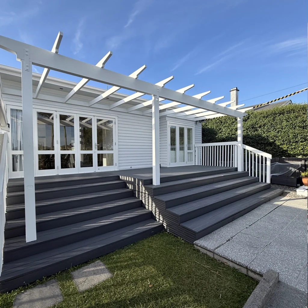 The image portrays a well-kept house exterior in Auckland's Bayswater neighbourhood. The new layer of paint enhances the house's architectural characteristics, giving it a clean, modern, and stylish appearance. The walls are painted in a smooth, neutral tone that is well complemented by crisp white trim and window frames that add contrast and elegance. The doorway is pleasant and complements the newly renovated exterior. The beautiful finish displays excellent craftsmanship, considerably boosting the home's street appeal while remaining well-kept and fashionable.