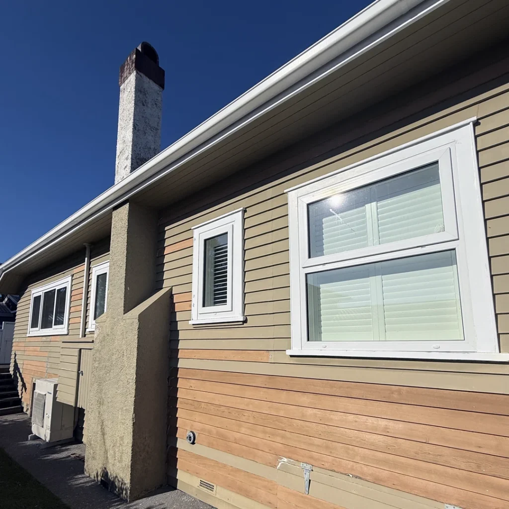 The image showcases a beautifully repainted house exterior in Bayswater, Auckland. The fresh coat of paint enhances the home’s classic architecture, giving it a clean, modern, and well-maintained look. The walls are finished in a smooth, neutral shade, complemented by crisp white trim and window frames that add contrast and sophistication. The front entrance is inviting, blending seamlessly with the refreshed exterior. The professional craftsmanship is evident in the flawless finish, significantly boosting the home’s curb appeal and making it look elegant and polished.