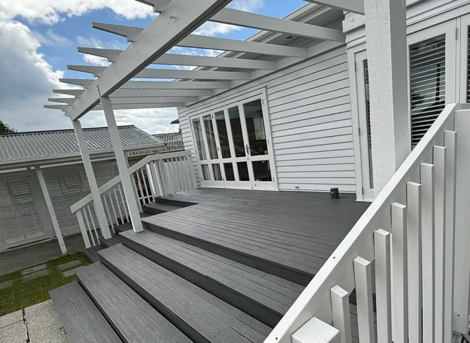 The image portrays a well-kept house exterior in Auckland's Bayswater neighbourhood. The new layer of paint enhances the house's architectural characteristics, giving it a clean, modern, and stylish appearance. The walls are painted in a smooth, neutral tone that is well complemented by crisp white trim and window frames that add contrast and elegance. The doorway is pleasant and complements the newly renovated exterior. The beautiful finish displays excellent craftsmanship, considerably boosting the home's street appeal while remaining well-kept and fashionable.